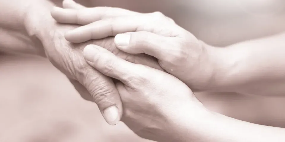 Caregiver, career hand holding elder hand in hospice care. 